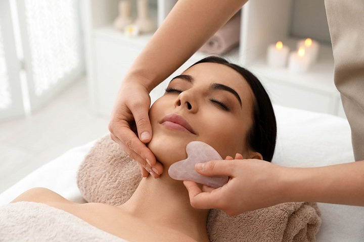 piękna młoda kobieta podczas masażu kamieniem gua sha w salonie kosmetycznym